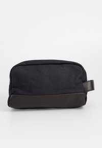 Musta kangasinen toilettilaukku, jossa on ruskea nahkapohja ja sivukahva. Laukulla on suorakaiteen muotoinen muoto ja vetoketjukiinnitys, joka mahdollistaa helpon käytön.