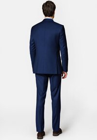 Granatowy garnitur, dopasowany krój, fakturowana tkanina, pojedyncze rozcięcie, pasujące spodnie, brązowe buty, widoczne detale szycia.