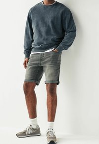 Sudadera gris con cuello redondo, combinada con pantalones cortos de mezclilla gris claro y zapatillas grises, con detalles en blanco y puños enrollados.