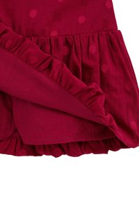 Tissu rouge avec une texture subtile à pois et des bords froncés, montrant des détails superposés et froncés.