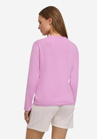 Maglione rosa chiaro a maniche lunghe con scollo rotondo, texture liscia e dettagli a coste, abbinato a pantaloni corti bianchi con texture.