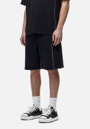 Schwarze Shorts mit weißen Nähdetails, aus weichem Stoff, kombiniert mit schwarz-weißen Sneakern und gerippten weißen Socken.