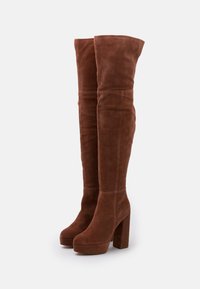 Botas de ante marrón hasta la rodilla con plataforma y tacón cuadrado. El diseño es suave, con una forma ligeramente holgada y sin herrajes visibles.