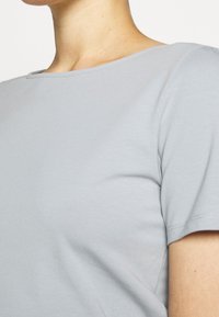 Lys grå kortærmet top med rund halsudskæring. Lavet af blødt, glat stof med en let glans og sømløs syning langs kanterne.