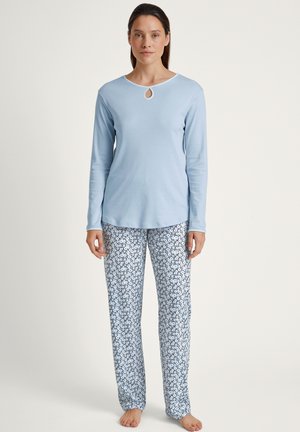 Hellblaues Langarmoberteil mit einem Schlüsselrand-Ausschnitt, kombiniert mit weißen Hosen mit einem blauen Blumenmuster. Weiche Stofftextur.
