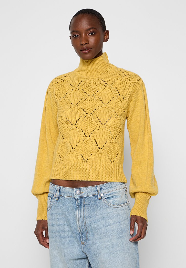 Maglione giallo a collo alto con motivi a diamante, maniche lunghe a sbuffo e polsini a coste, abbinato a jeans in denim blu chiaro.