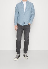 Chemise bleu clair à manches longues dans une coupe décontractée, associée à un jean gris foncé et des baskets montantes noires avec des lacets blancs. Look simple et décontracté.