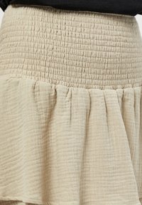 Bežna krilna krila iz mehkega, teksturiranega materiala. Zgornji del ima smock dizajn, ki prehaja v razširjen, nabrani spodnji del.
