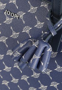 Marineblå håndtaske med en tekstureret læderoverflade, der har et hvidt blomsterdesign og en dekorativ foldet detalje på siden.