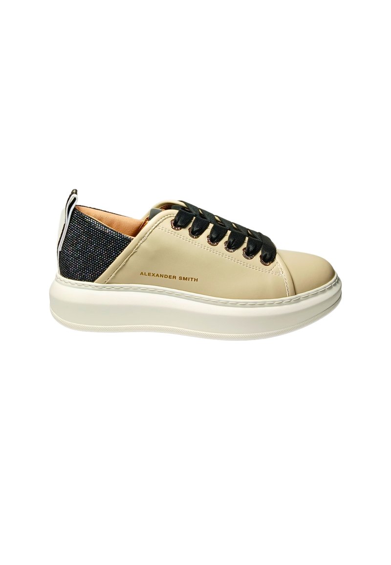 Beige leren sneakers met een zwarte gepatterneerde achterkant, ronde neus en zwarte veters. Heeft een dikke witte rubberen zool en subtiele branding.