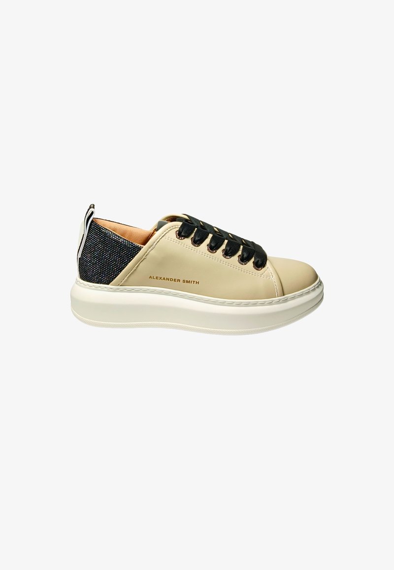Beige leren sneakers met een zwarte gepatterneerde achterkant, ronde neus en zwarte veters. Heeft een dikke witte rubberen zool en subtiele branding.