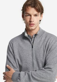 Grå zip-up tröja i stickad kvalitet med hög krage. Har en mjuk yta och en liten dragkedja vid halsen.