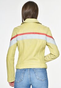 Leren jack in het geel met rode en witte diagonale strepen over de rug. Heeft een getailleerd ontwerp en een gladde textuur.