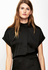 Zwarte satijnen top met een hoge halslijn, korte opgerolde mouwen en een gladde, strakke textuur. Beschikt over een eenvoudig, clean ontwerp.