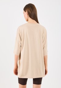 T-shirt oversized bege com mangas curtas, feita de tecido suave. Apresenta um decote redondo e um corte descontraído, estilizada com calções de ciclista escuros.