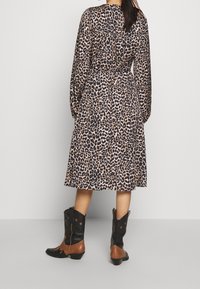 Klänning med leopardmönster, långa ärmar, åtsittande midja och flödande kjol. Kombinerad med svarta och bruna cowboyboots med stjärndetaljer.