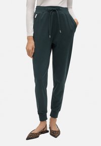 Joggers verde oscuro con cintura ajustable, bolsillos laterales y puños acanalados. Llevados con unos zapatos planos de punta de estampado de leopardo.