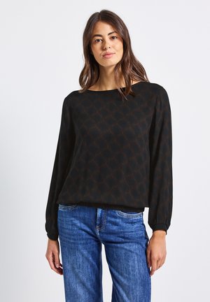 Sort langærmet bluse med geometrisk brunt mønster, rund halsudskæring og let rynkede ærmer. Sammen med blå denim jeans.