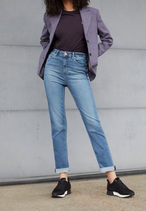 Lyseblå højtaljede jeans med opkrøllede manchetter, parret med en sort top og en grå ternet blazer, suppleret af sorte sneakers.