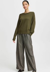 Olivgrüner, gestrickter Pullover mit rundem Halsausschnitt, kombiniert mit grauen, weit geschnittenen Hosen. Das Outfit verfügt über gerippte Bündchen und einen lockeren Schnitt.