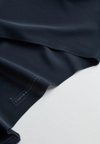 Tejido azul marino con una textura suave que presenta un logotipo y etiqueta, destacando un diseño ligero y elástico adecuado para ropa deportiva.