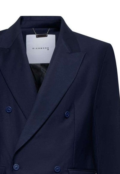 Blazer doppiopetto blu navy con revers affilati, dotato di due bottoni e una fodera interna pulita. Etichetta con marchio visibile all'interno.