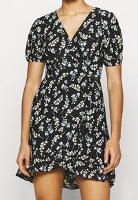 Černé zavinovací šaty s krátkými balónovými rukávy, s květinovým vzorem v světle modré a krémové barvě, a volánkovým lemem. Vyrobeno z lehkého materiálu.