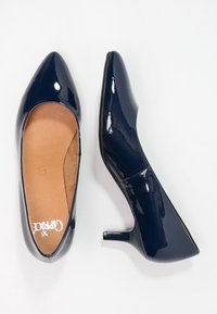 Chaussures à talon en cuir verni bleu marine avec un bout pointu et un talon aiguille modéré, présentant une finition lisse et une semelle intérieure rembourrée.