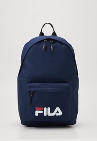 Zaino blu navy con una superficie liscia, dotato di una tasca frontale con zipper e logo FILA bianco. Doppie cerniere superiori e manico di trasporto rinforzato.