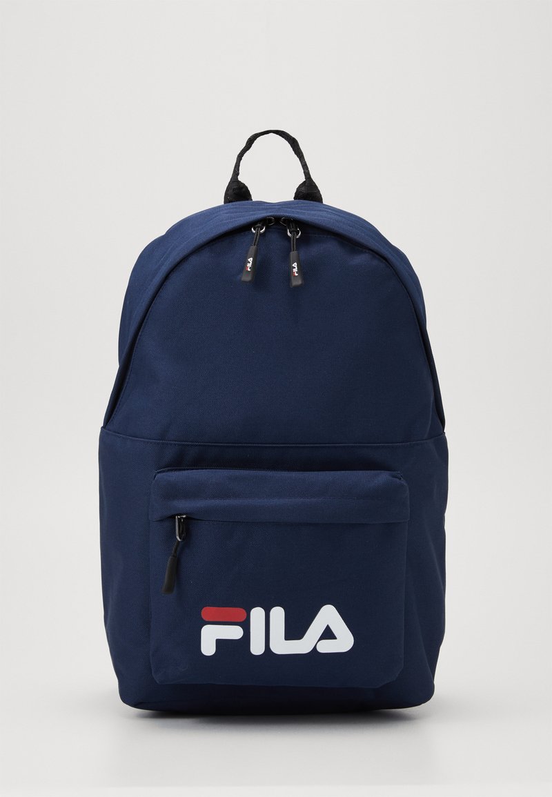 Zaino blu navy con una superficie liscia, dotato di una tasca frontale con zipper e logo FILA bianco. Doppie cerniere superiori e manico di trasporto rinforzato.