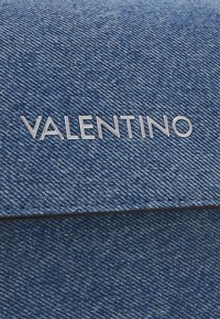 Džínová taška přes rameno s metalickým stříbrným nápisem "VALENTINO" na klopě, s texturovanou modrou látkou a černými švy.