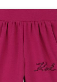 Fuchsia joggingbroek met elastische tailleband, met subtiele plooien en een zwarte "Karl" logo versiering. Zachte, gladde stoftextuur.