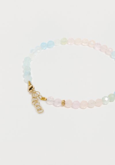 Bracelet extensible avec petites perles facettées de couleurs pastel et fermoir en métal doré avec chaîne d'extension sur fond blanc.