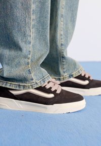 Black and suede sneakers with light pink laces and white accents; worn with light blue, slightly loose-fitting denim pants.