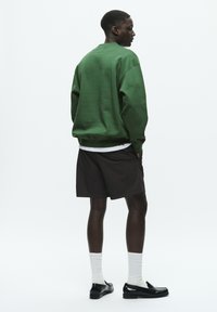 Green sweatshirt, black shorts, white crew socks, and black shoes. Material appears smooth; design is casual with relaxed fit.