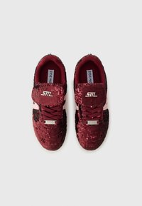 Red and black sequined sneakers with a rounded toe, thick maroon laces, and silver branding on the tongue. Textured, shiny surface.