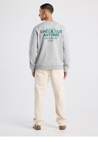 Harmaa collegepaita, jossa vihreällä takana teksti "CHECK OUT ANYTIME." Yhdistetty kermanvärisiin housuihin ja ruskeisiin kenkiin.