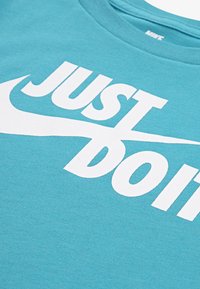 Turkis bomull t-skjorte med rund hals og en stor hvit "JUST DO IT"-logo. Glatt tekstur og korte ermer.