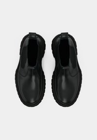 Par de botas pretas de couro slip-on com solas de borracha grossas, painéis laterais elásticos e alças de puxar, vistas de cima sobre um fundo simples.