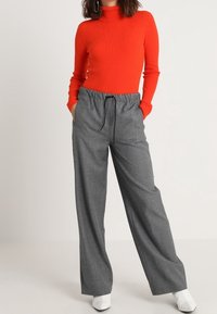 Pull rouge à col roulé côtelé associé à un pantalon gris taille haute à jambes larges, avec une taille à cordon de serrage et une texture de tissu lisse.