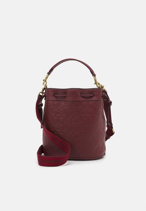 Bordowa skórzana torba typu bucket z wytłoczonym wzorem logo, krótkim uchwytem i regulowanym paskiem na ramię z akcentami w czerwonym kolorze.