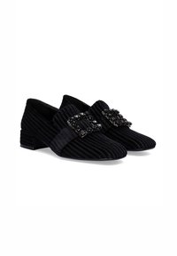 Mocasines de pana negros con tacón plano, que presentan una hebilla decorativa con embellishments negros y textura acanalada en la parte superior.