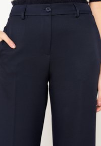 Námořnické oblekové kalhoty z texturované tkaniny se straight fit střih. Mají zapínání na knoflík, poutka na opasek a boční kapsy.