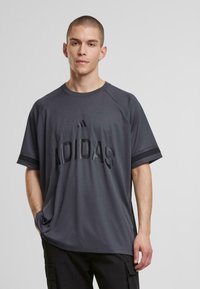 Tumehall lühikeste varrukatega T-särk, mis on valmistatud tekstuuriga kangast, millel on reljeefne "ADIDAS" logo ja kontrastsed triibud varrukatel.