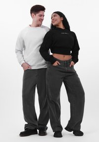 To modeller står side om side, iført en hvid tekstureret sweatshirt og en sort cropped hoodie, begge parret med løse sorte jeans.