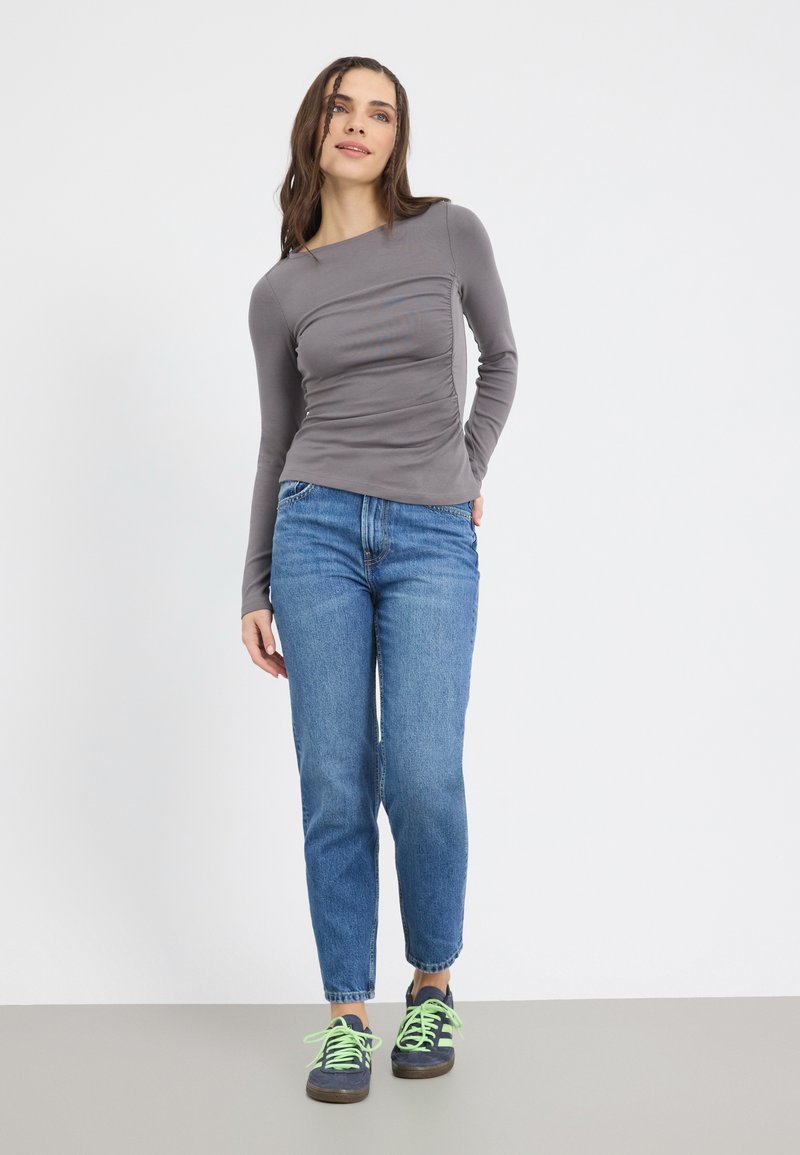 Gray long-sleeve fitted top with side ruching, paired with high-waisted blue jeans and black sneakers with green laces. Smooth texture.
