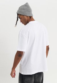 Camiseta blanca de algodón con mangas cortas y corte holgado. Llevada con un gorro gris de canalé, con un peinado trenzado y acentos decorativos.