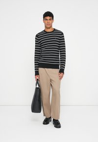 Maglione a righe bianco e nero, pantaloni beige, scarpe nere, con una borsa tote nera. Abbigliamento casual con una vestibilità rilassata.