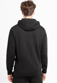 Sudadera de algodón negra, vista trasera. Cuenta con una capucha amplia, mangas largas y puños de canalé. Textura suave con un diseño de corte relajado.