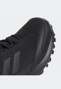Gros plan de l'avant d'une chaussure de sport noire avec dessus en synthétique texturé et mesh, lacets noirs et semelle à relief robuste.
